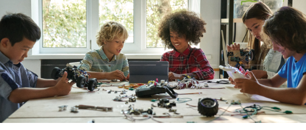 Multiracial school kids students making robotic cars using tablet computer. Diverse junior children pupils building robot vehicle learning at table at STEM code ai engineering science education class.